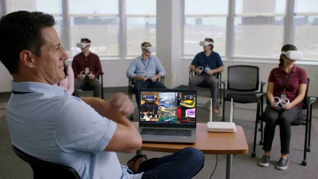 A trainer stays seated and follows every learner's headset view on a laptop running OmnicastVR, next to a Wi-Fi router